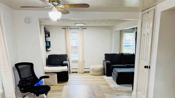 A spacious living area with a wooden dining table, two benches, a black office chair, a sofa, and a ceiling fan. - Super Modern 2-Bedroom Riverside Home @ RIT (Rochester)