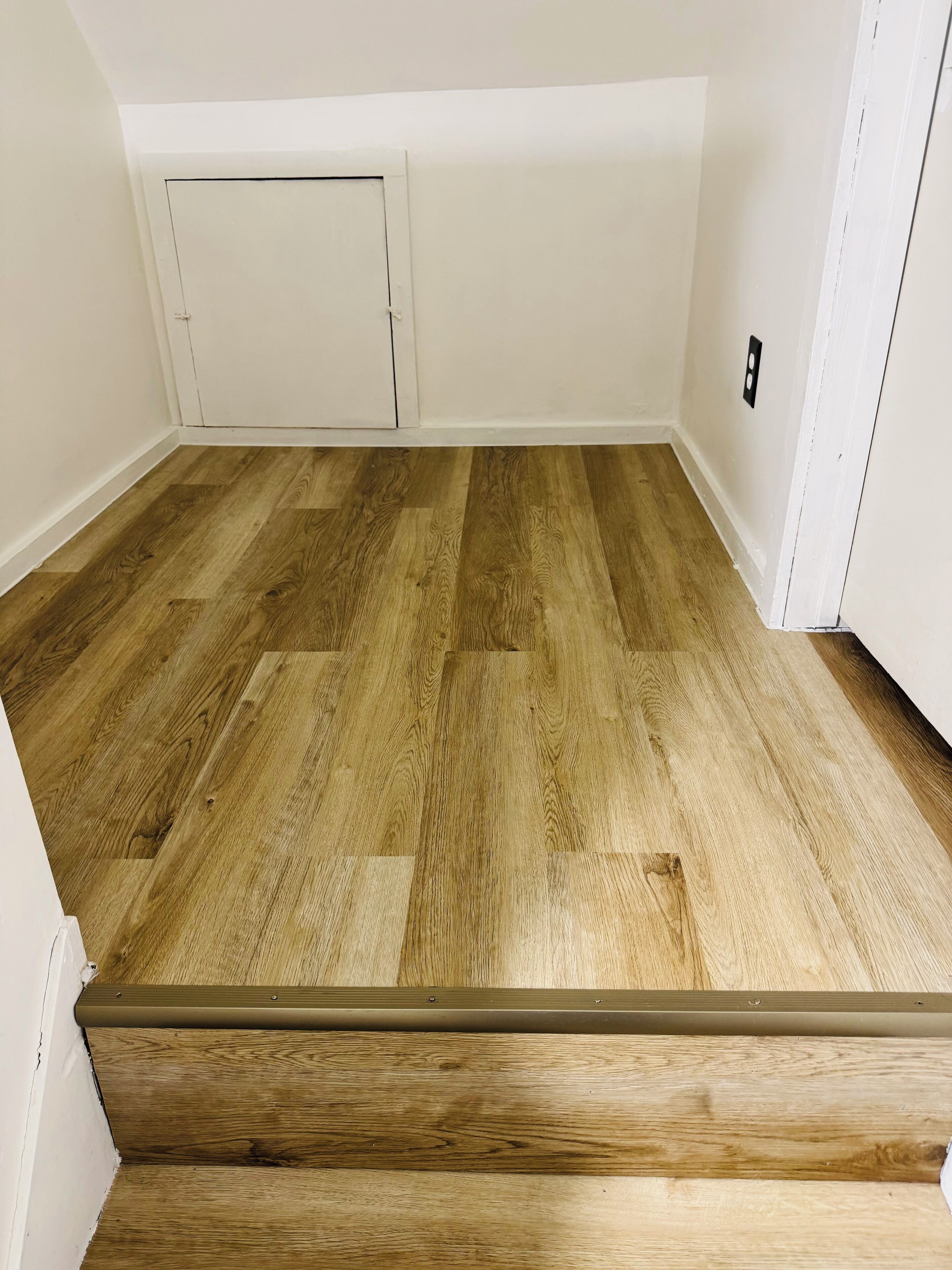Um quarto com piso de madeira, paredes brancas e uma porta com uma pequena janela.