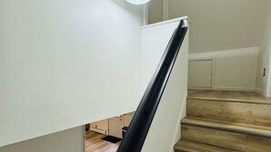 A staircase with wooden steps and a black handrail, leading to a landing with a white door and a light fixture. - Super Modern 2-Bedroom Riverside Home @ RIT (Rochester)