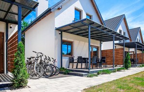 Une maison moderne dotée d’un patio couvert, avec des vélos garés à l’extérieur et un petit jardin.