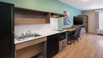 Una cocina compacta con lavamanos, microondas y un comedor con una silla y mesa.