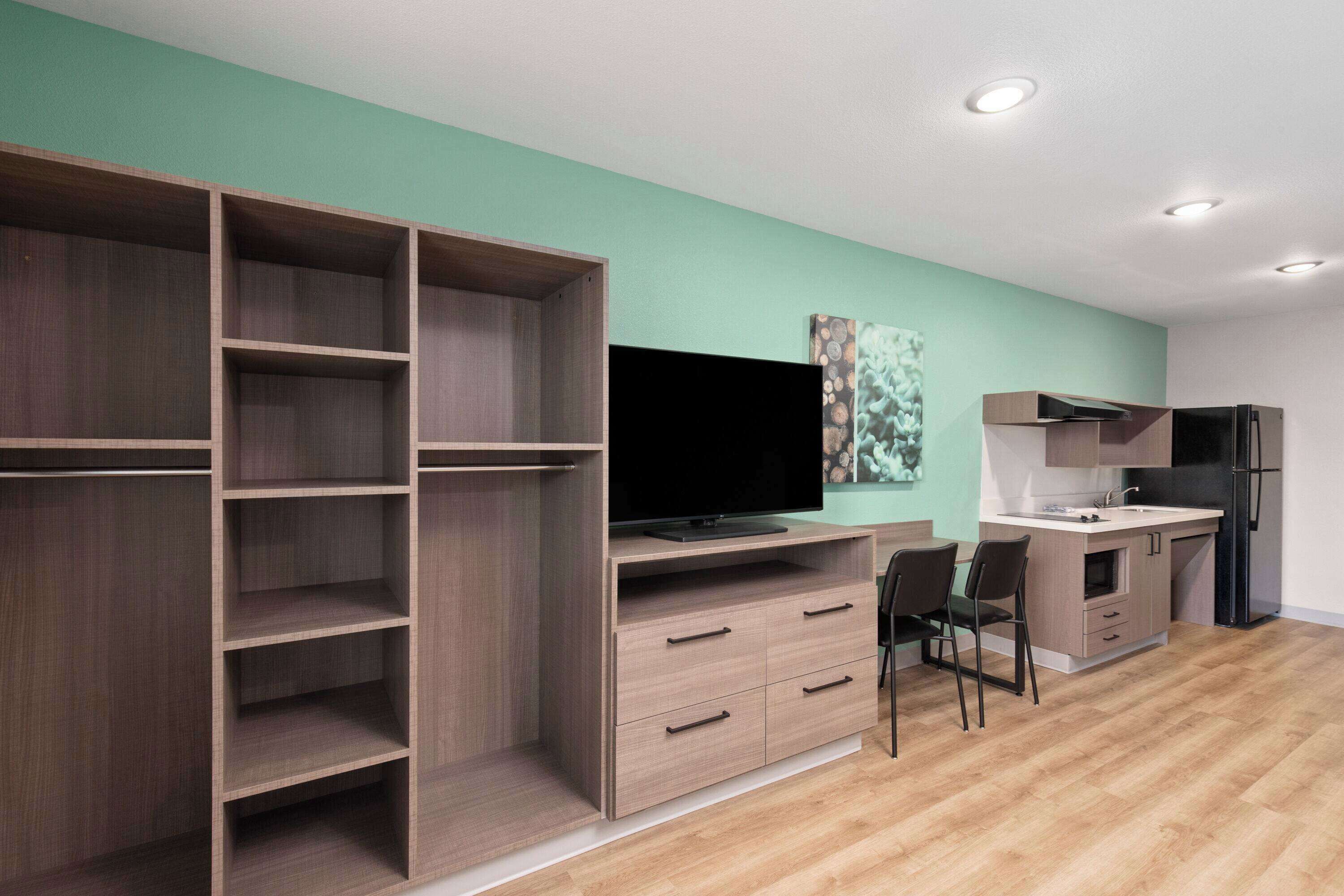 A modern living room with a TV, wooden shelving, a dining area, and a kitchen.