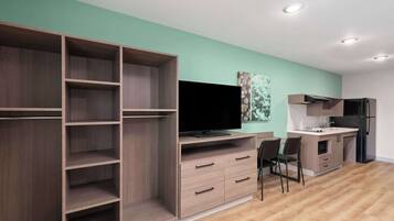 A modern living room with a TV, wooden shelving, a dining area, and a kitchen.