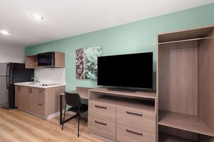 Una cocina compacta con microondas, lavamanos y un televisor de pantalla plana sobre un escritorio de madera.