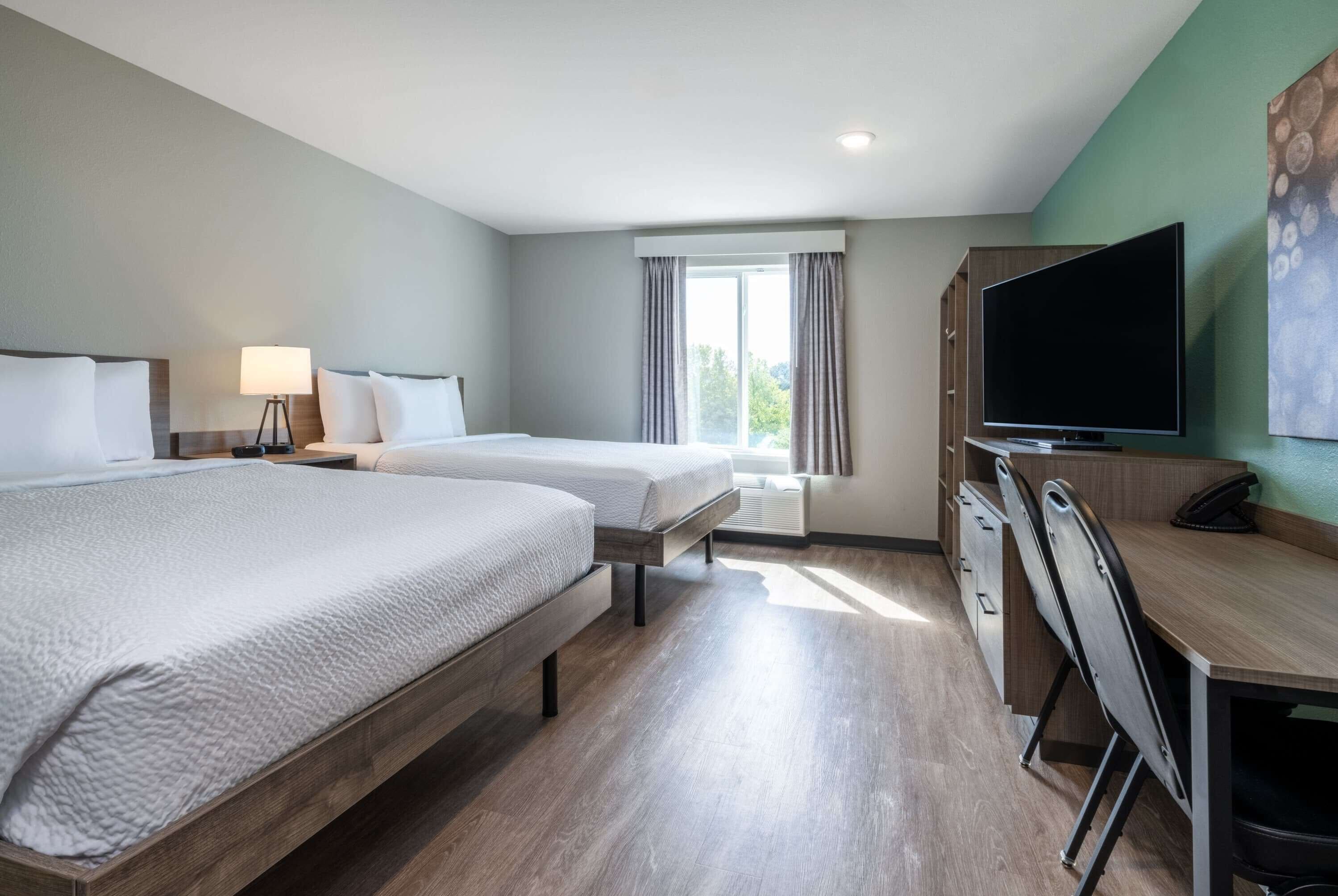 Habitación de hotel con dos camas, un escritorio, un televisor y una ventana con cortinas.