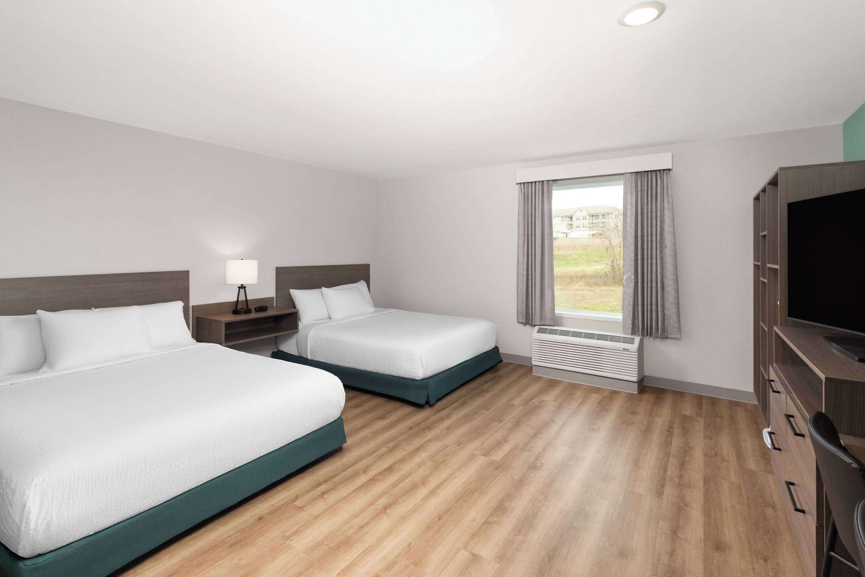 Habitación de hotel con dos camas, televisión, escritorio y ventana con cortinas.