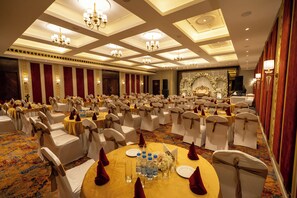 A banquet hall with round tables, white chairs, chandeliers, and a stage with floral decorations. - Ramada Encore By Wyndham Rajbagh Srinagar (Srinagar)