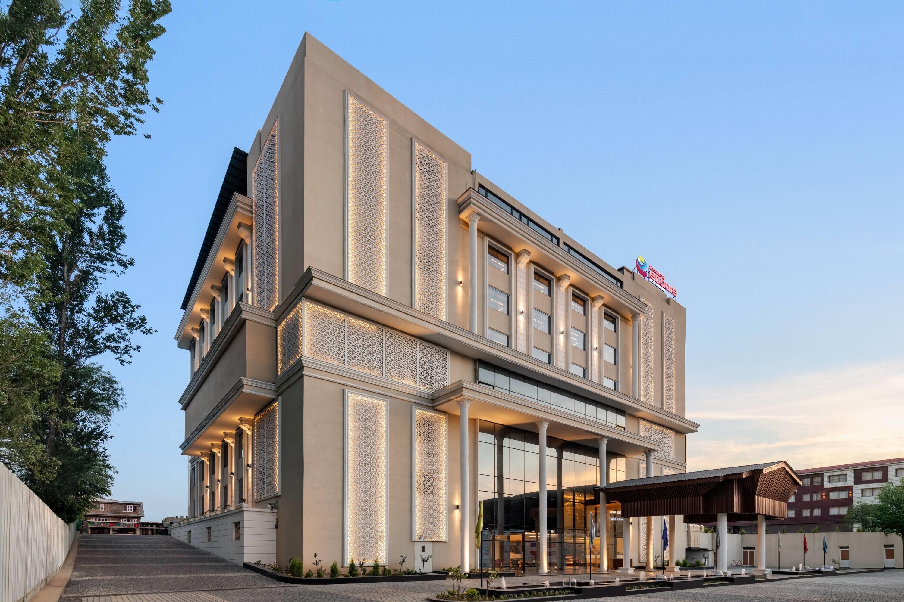 A modern hotel with a prominent entrance, large windows, and decorative lighting.