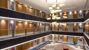 A multi-level hotel lobby with a central seating area, wooden paneling, and modern chandeliers. - Ramada Encore By Wyndham Rajbagh Srinagar (Srinagar)