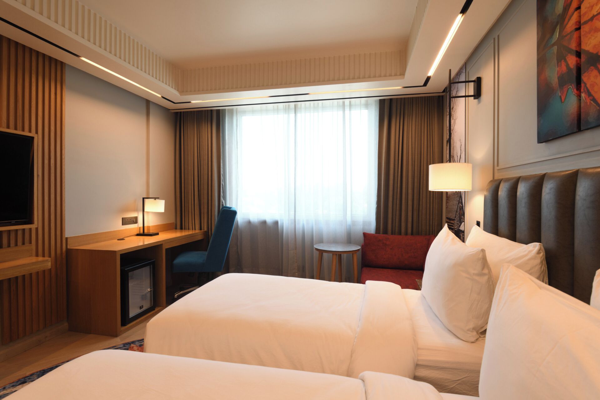 Una habitación de hotel con una cama, un escritorio, una silla, un televisor y un cuadro en la pared.