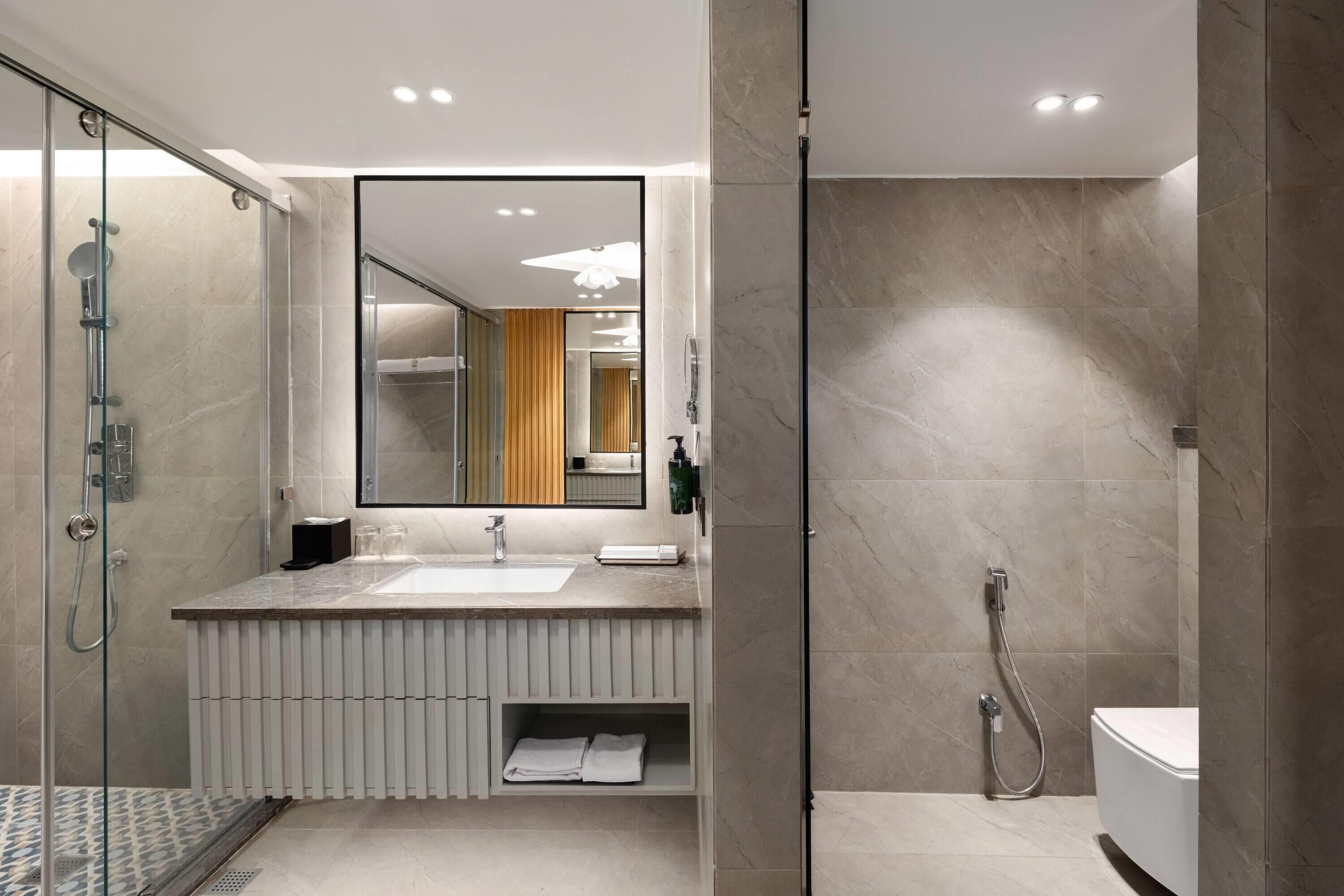 A modern bathroom with a glass-enclosed shower, a large mirror, and a white vanity with a sink.