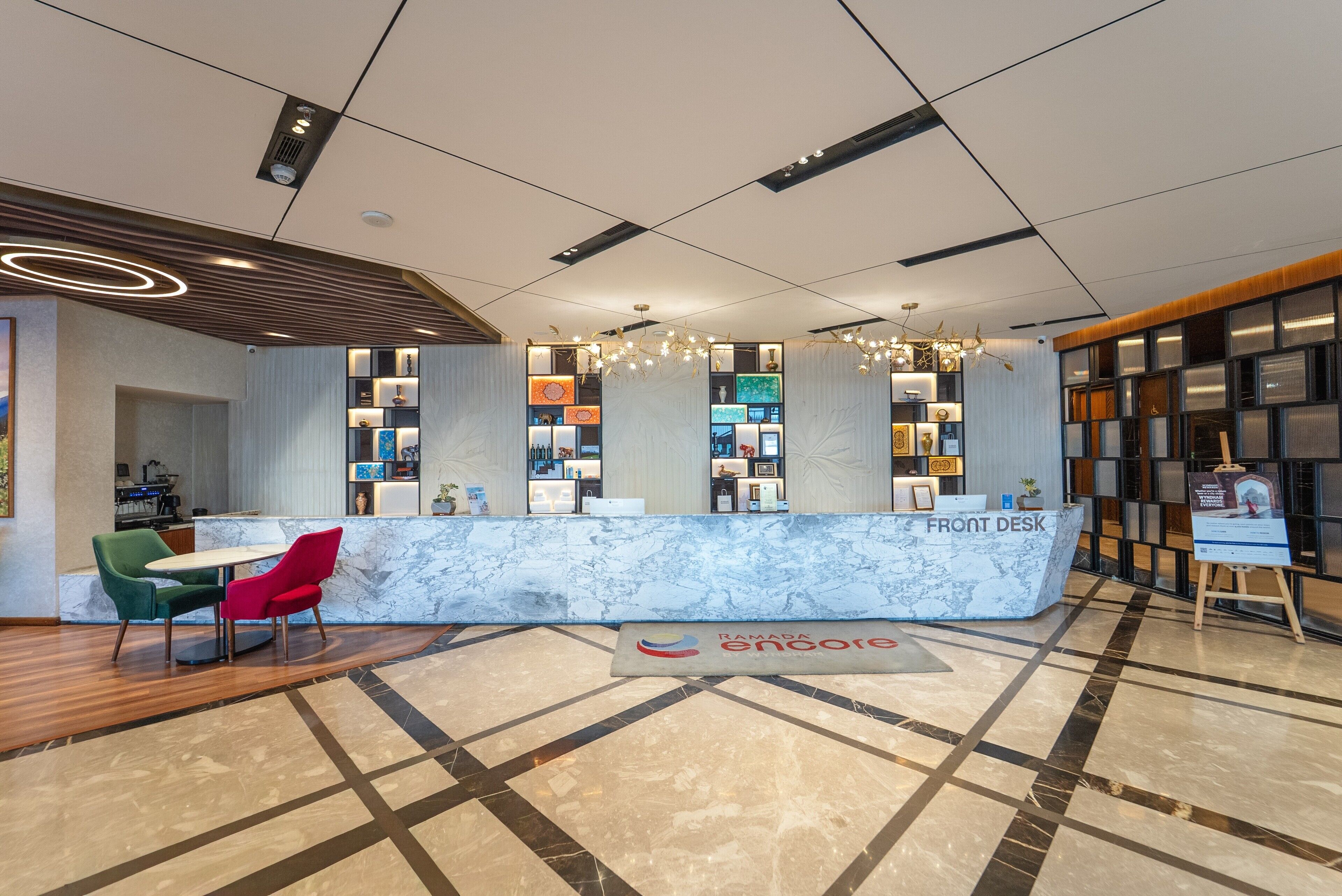 A modern reception area with a marble counter, a front desk, and a seating area with green and red chairs.