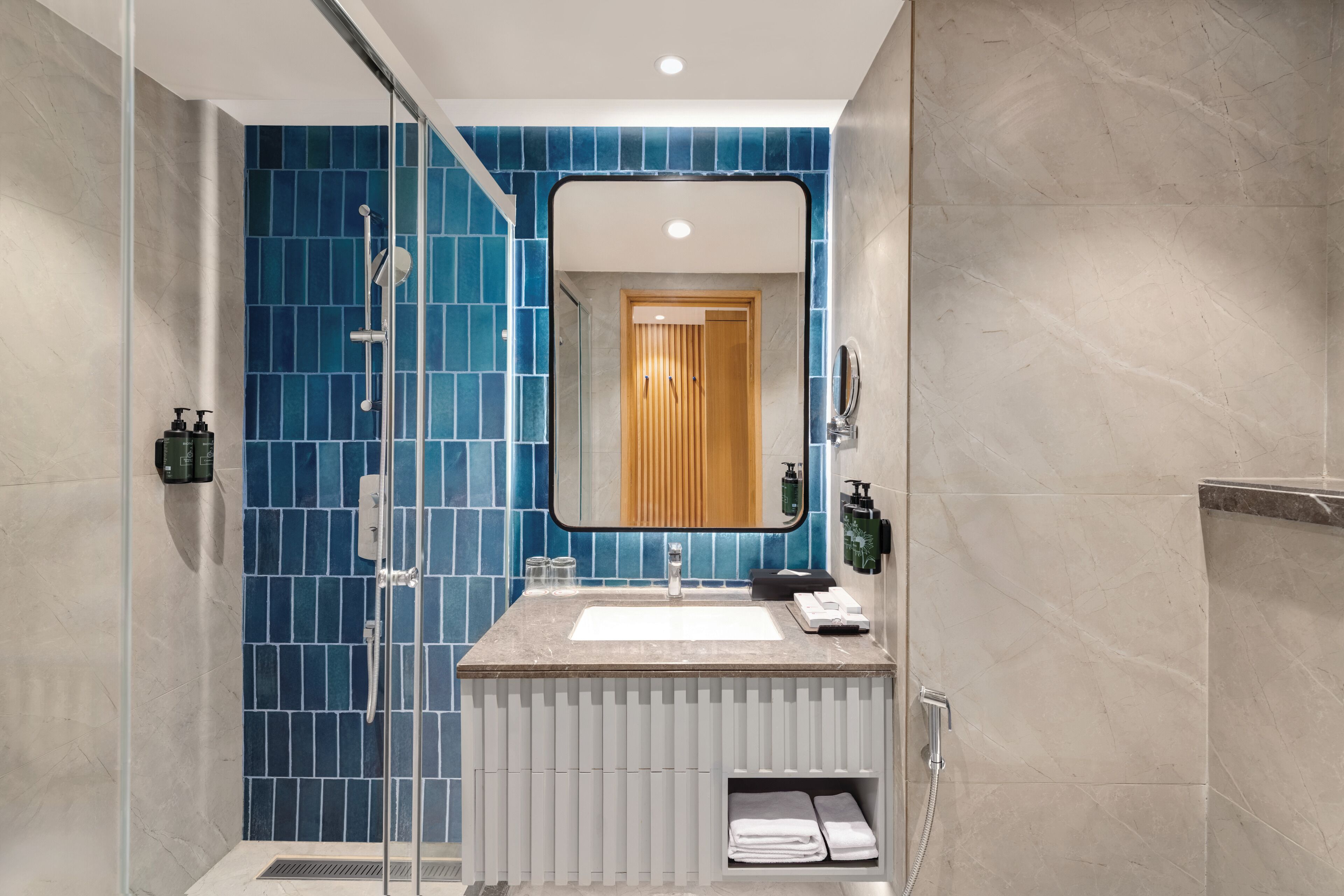 Un baño moderno con pared de ducha azul con azulejos, un lavabo blanco y un espejo encima.