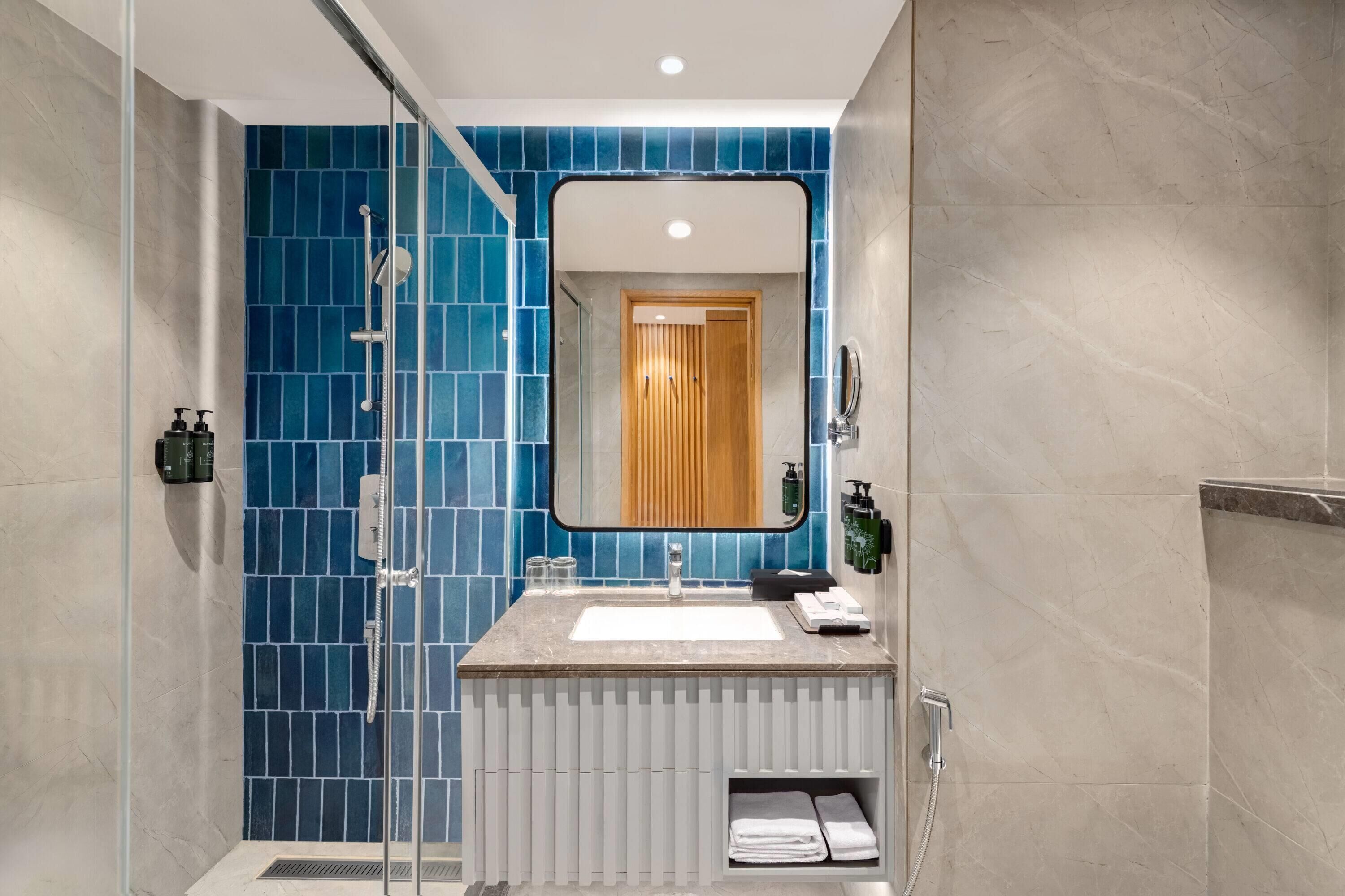 A modern bathroom with a glass-enclosed shower, a white sink, and a blue-tiled wall.