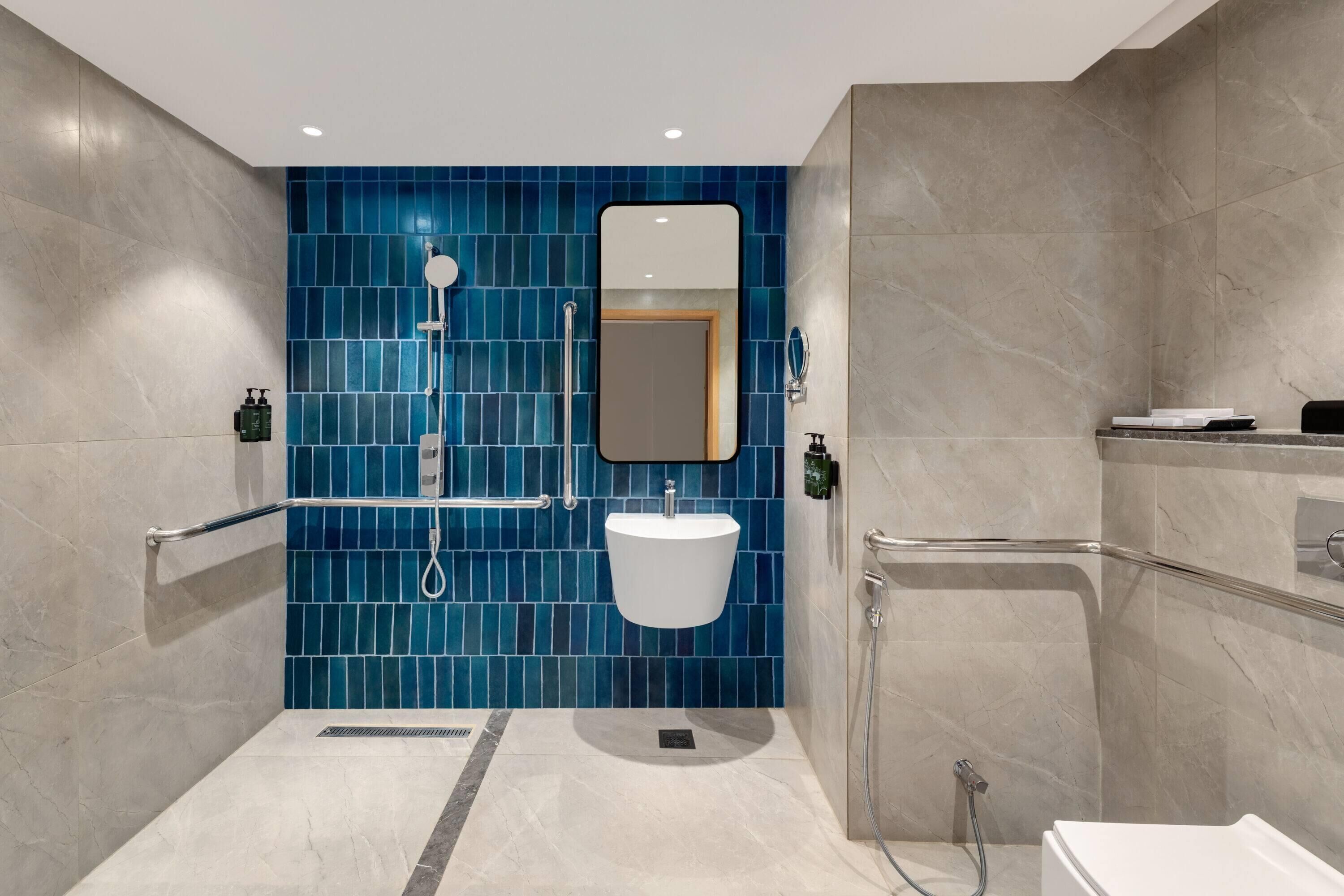 A modern bathroom with a blue-tiled shower wall, a white sink, and a mirror.