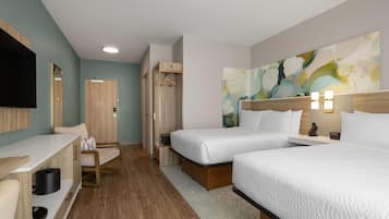 Habitación de hotel con dos camas, un escritorio, una silla, un televisor y un cuadro en la pared.