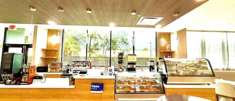 A coffee shop interior with a counter, coffee machines, a display case with pastries, and a sign that says 'Open Come in'.