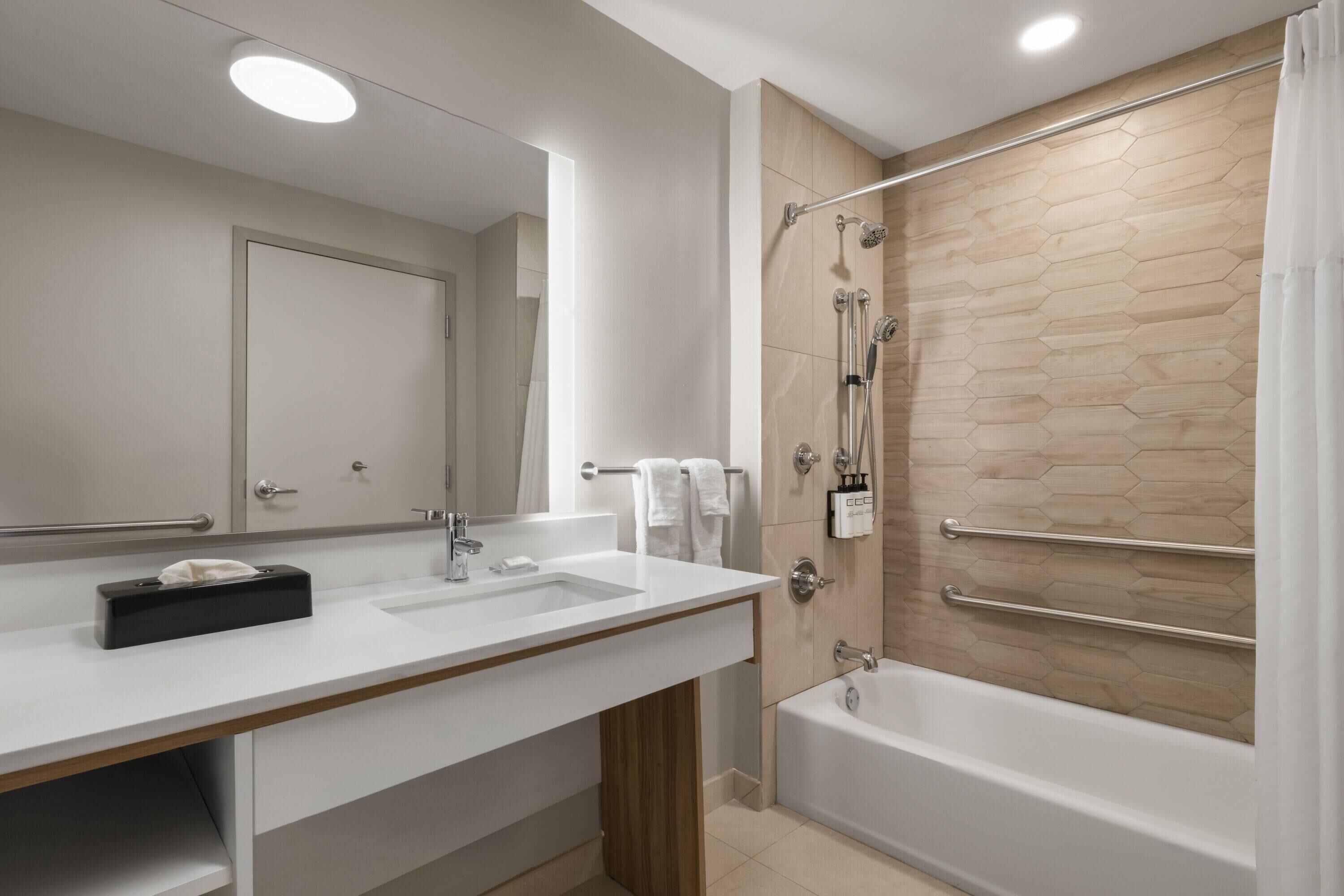 A modern bathroom with two sinks, a large mirror, a shower with a glass door, and a bathtub.
