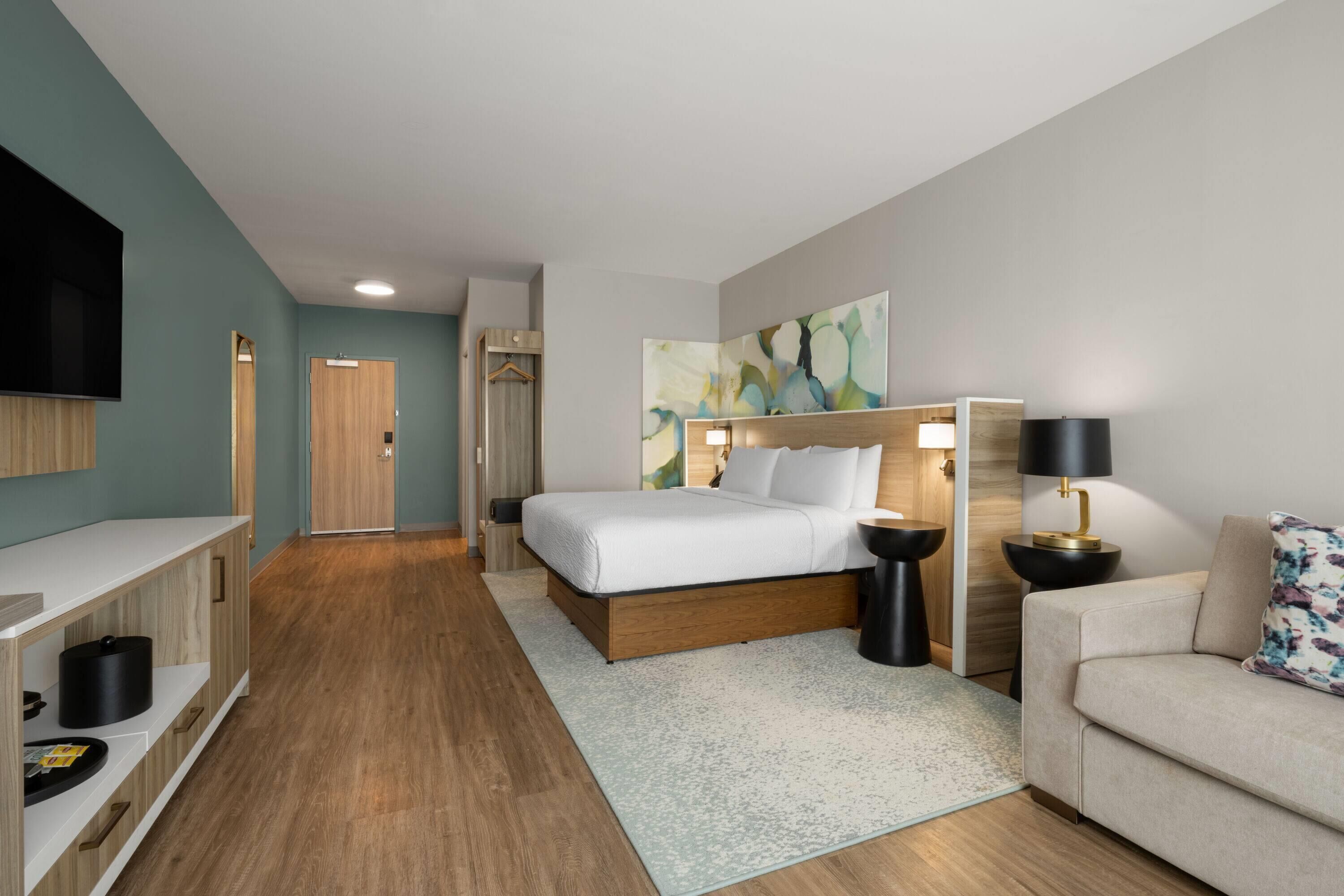 Une chambre d’hôtel moderne équipée d’un lit, d’une table de chevet, d’une lampe et d’un téléviseur fixé au mur.