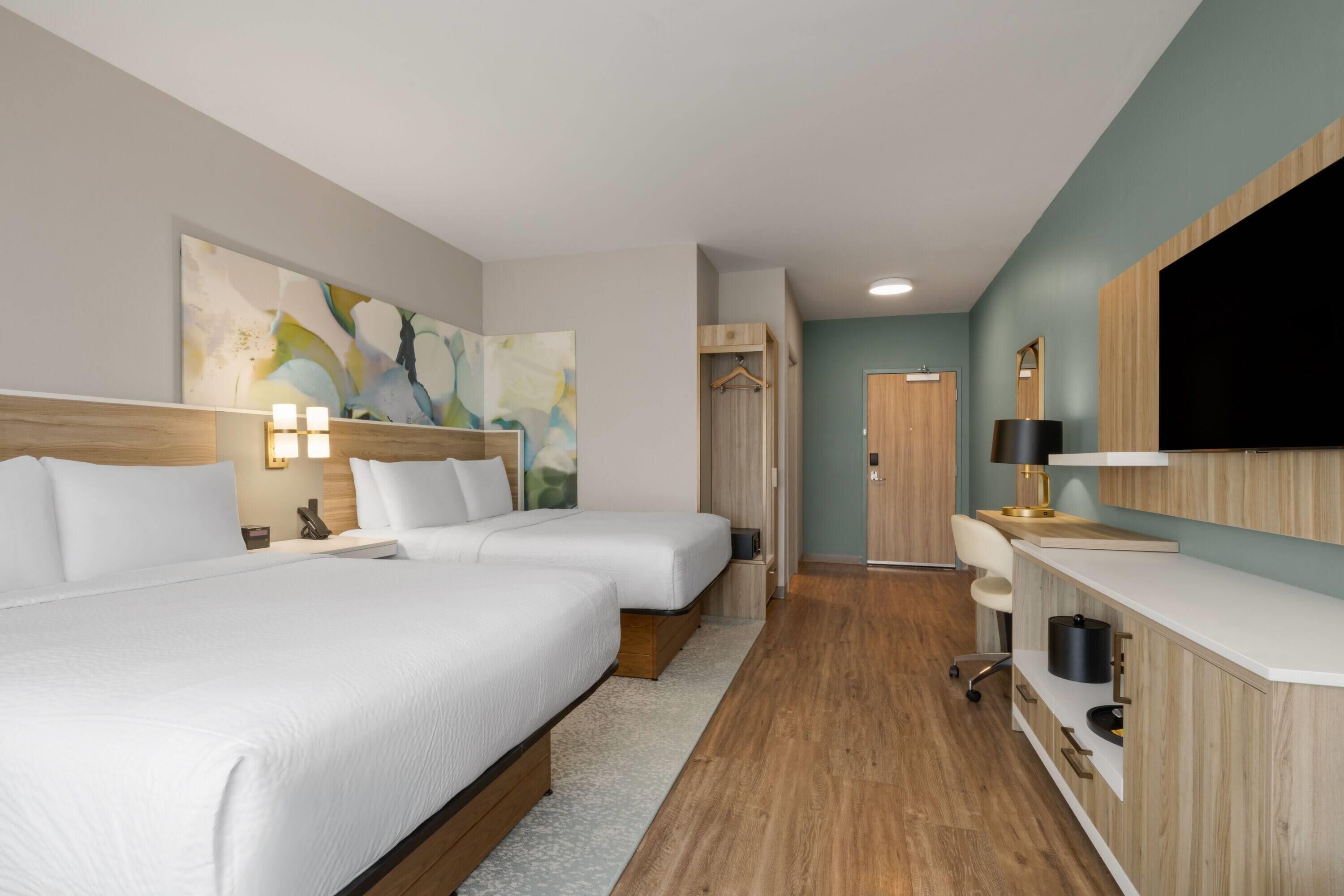 A hotel room with two beds, a desk, a TV, and a painting on the wall.