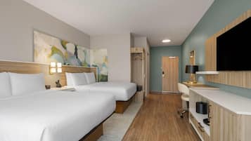 A hotel room with two beds, a desk, a TV, and a painting on the wall.