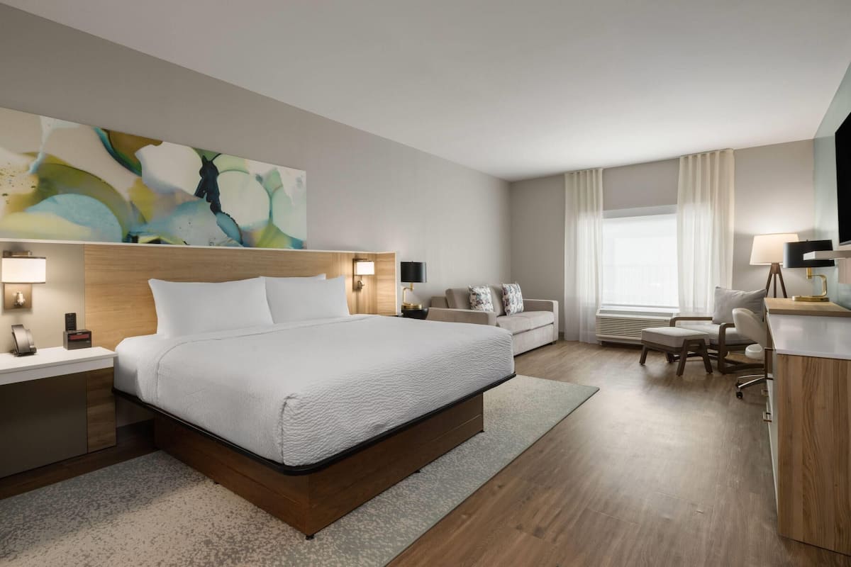Une chambre d’hôtel avec un grand lit, des tables de chevet, un bureau, une chaise et un canapé.
