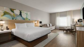 Ein Hotelzimmer mit einem großen Bett, Nachttischen, einem Schreibtisch, einem Sessel und einer Couch.