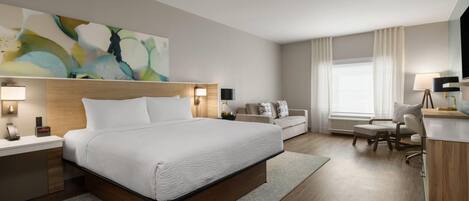 A hotel room with a large bed, bedside tables, a desk, a chair, and a couch.