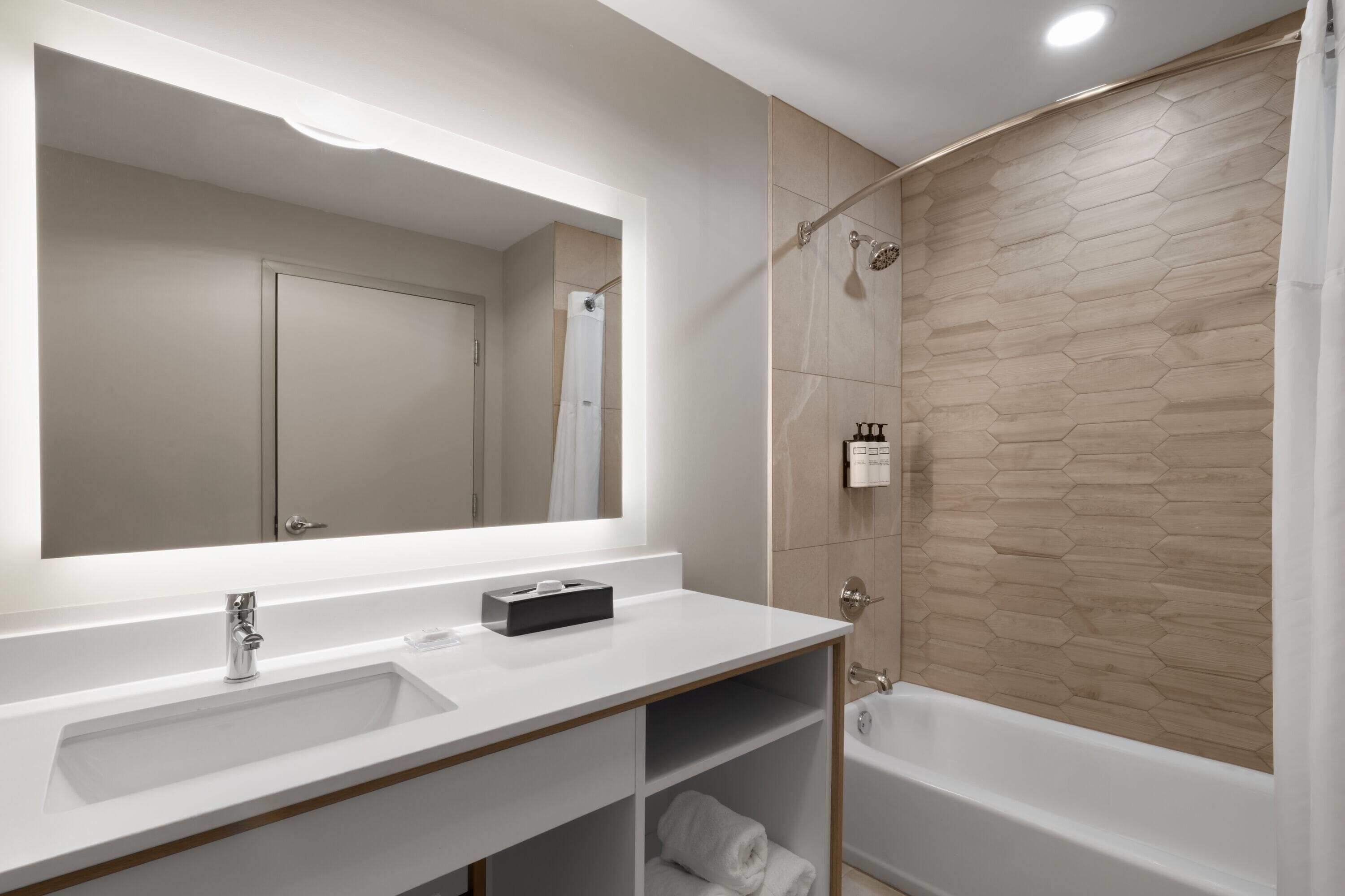 A modern bathroom with a large mirror, two sinks, a shower, and a bathtub.