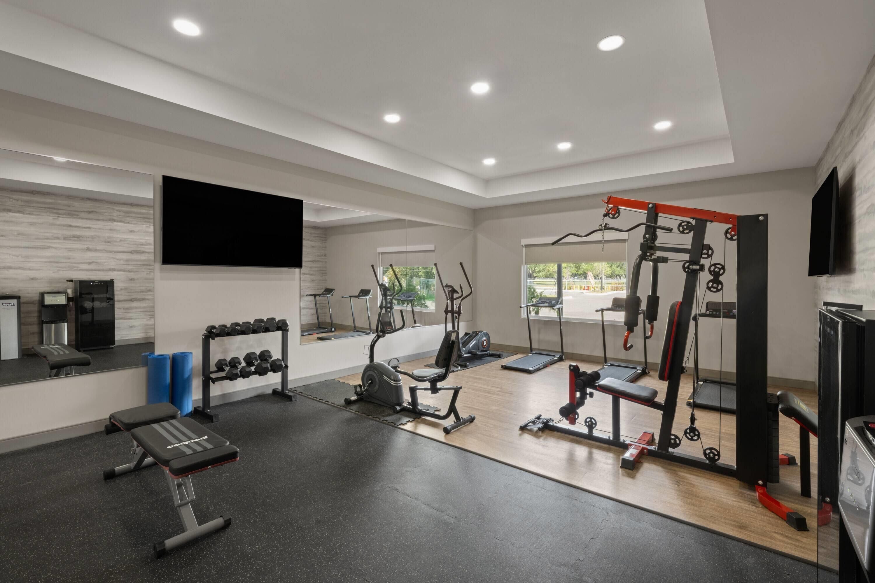 Academia moderna com diversos equipamentos de exercício, um banco, halteres e um espelho grande.
