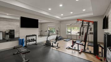 Academia moderna com diversos equipamentos de exercício, um banco, halteres e um espelho grande.