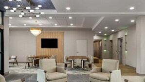 A modern conference room with a wooden table, beige chairs, a chandelier, and a flat-screen TV. - Wyndham Garden Tampa Fairgrounds/Casino (Tampa)