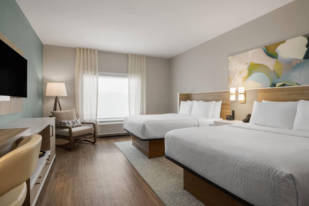 Une chambre d’hôtel avec deux lits, un bureau, une chaise, une télévision et un tableau au mur.