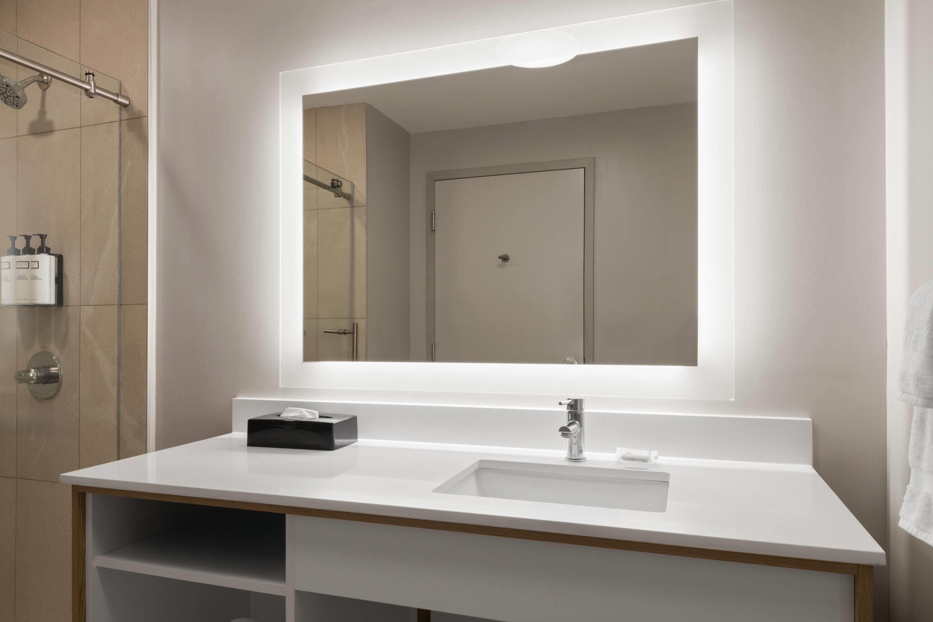 Uma casa de banho moderna com toucador branco, um espelho grande e zona de duche.
