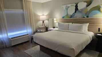 A hotel room with a large bed, a bedside table, a lamp, a wall-mounted TV, and a window with curtains.