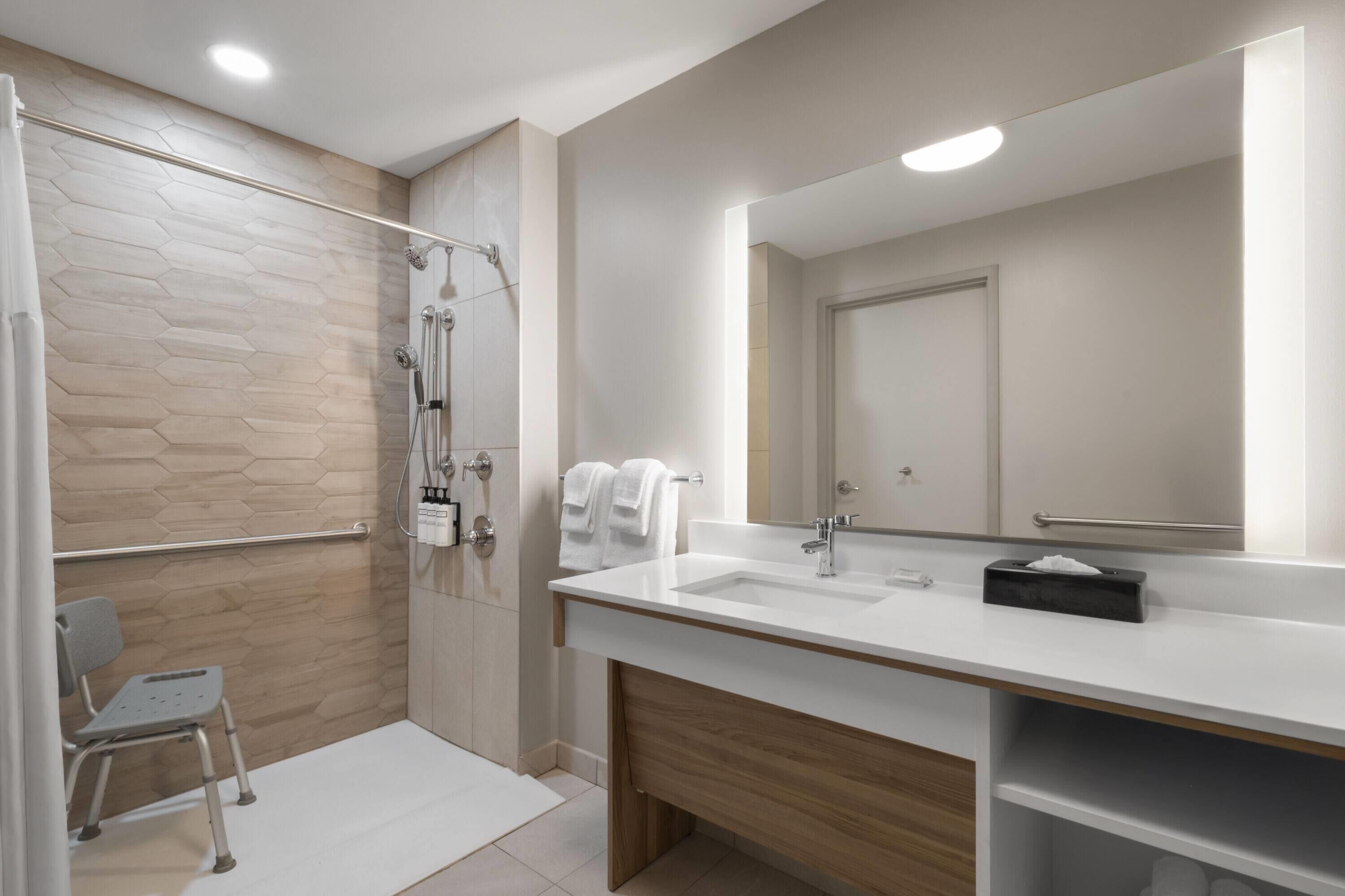 A modern bathroom with a shower, a sink, a mirror, and a chair.