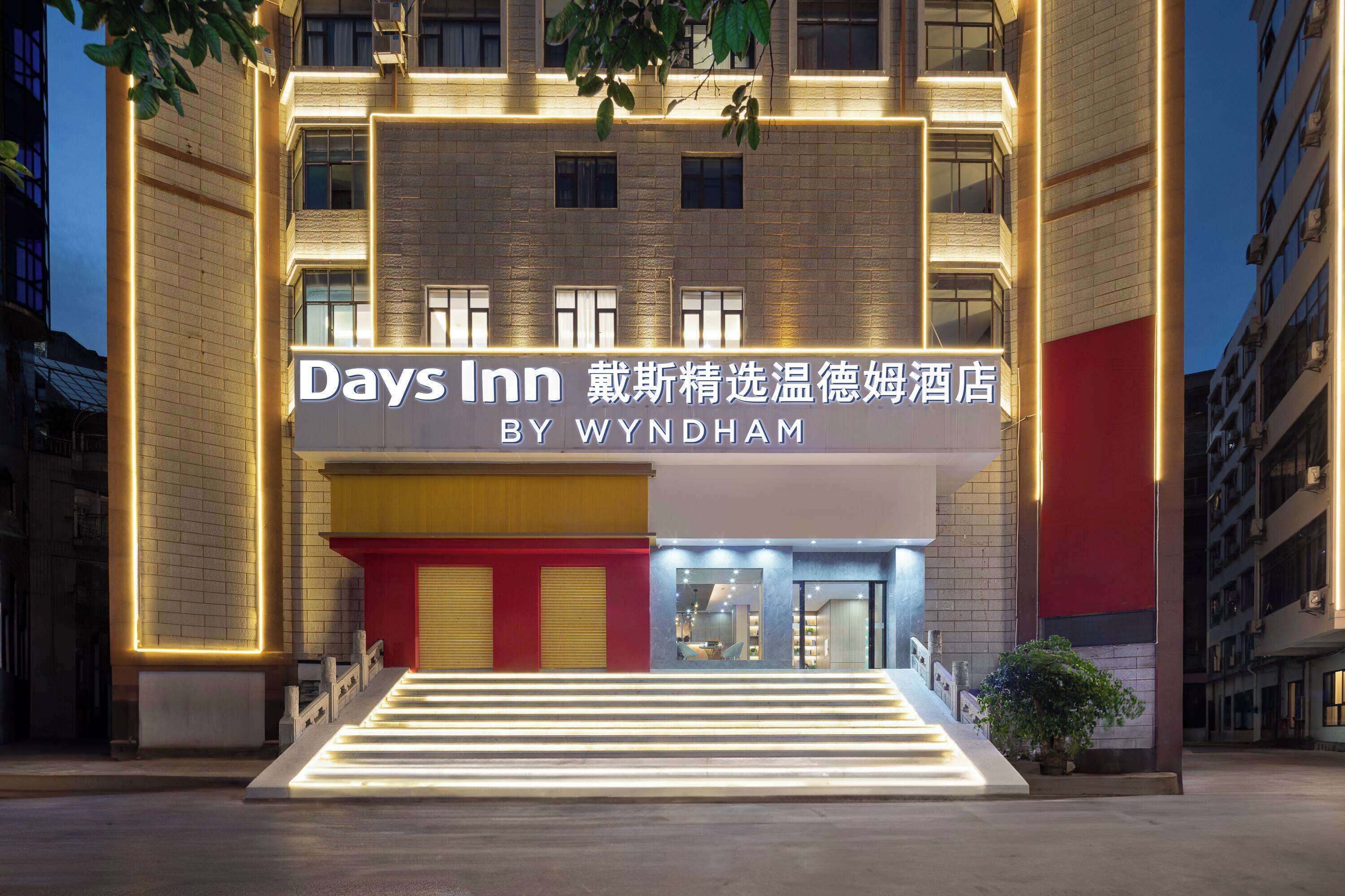 A hotel entrance with a sign for Days Inn by Wyndham, featuring a modern design with illuminated steps and a red and yellow facade.