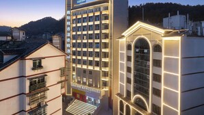 Un hotel de varios pisos con el letrero de Days Inn, que presenta una fachada moderna con líneas iluminadas, una entrada central y vistas de los edificios y colinas circundantes.