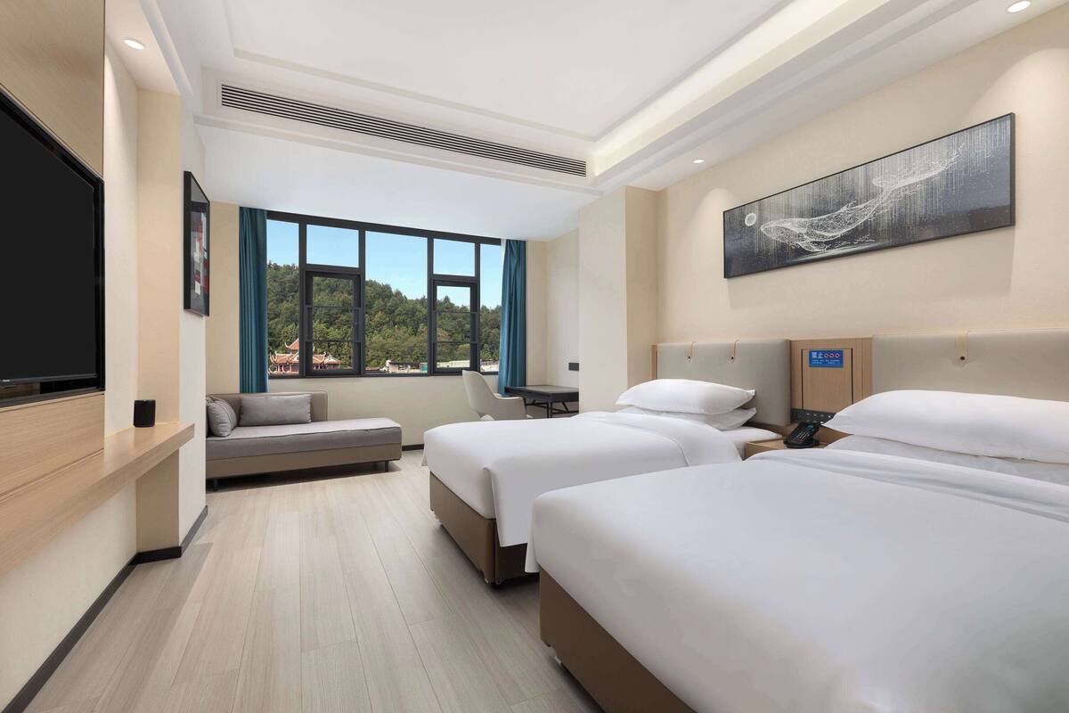 Une chambre d’hôtel avec deux lits, un canapé, une télévision et une grande fenêtre donnant sur l’extérieur.
