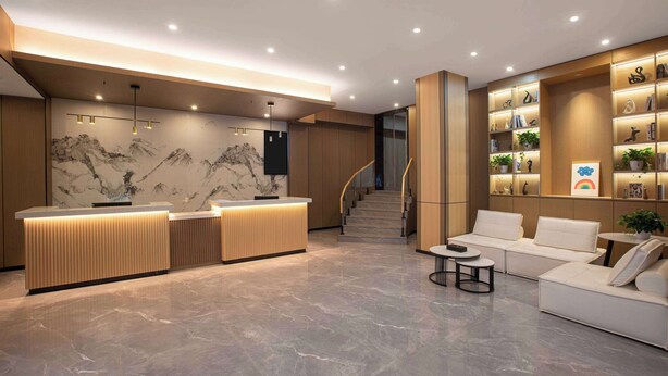 Un área de recepción moderna con un mostrador de mármol, una escalera y una zona de estar con un sofá blanco y una mesita redonda.