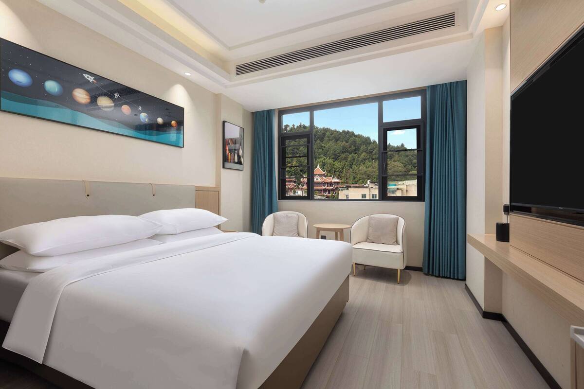 Une chambre d’hôtel avec un grand lit, une télévision, une petite table et une fenêtre donnant sur un bâtiment traditionnel.