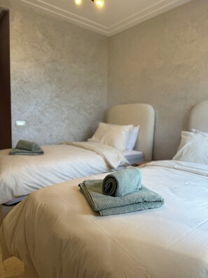 A hotel room with two beds, each with a white bedspread and pillows. There is a folded towel on the bed in the foreground. - Serenity Apartment: Self Check in, Tramway, Garage,wifi (Casablanca)