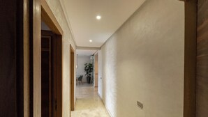 A hallway with a wooden door on the left, a potted plant in the distance, and a ceiling light.