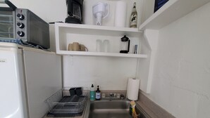 Een kleine keuken met een magnetron, koffiezetapparaat en een klein plankje met flessen en een alcoholische fles.