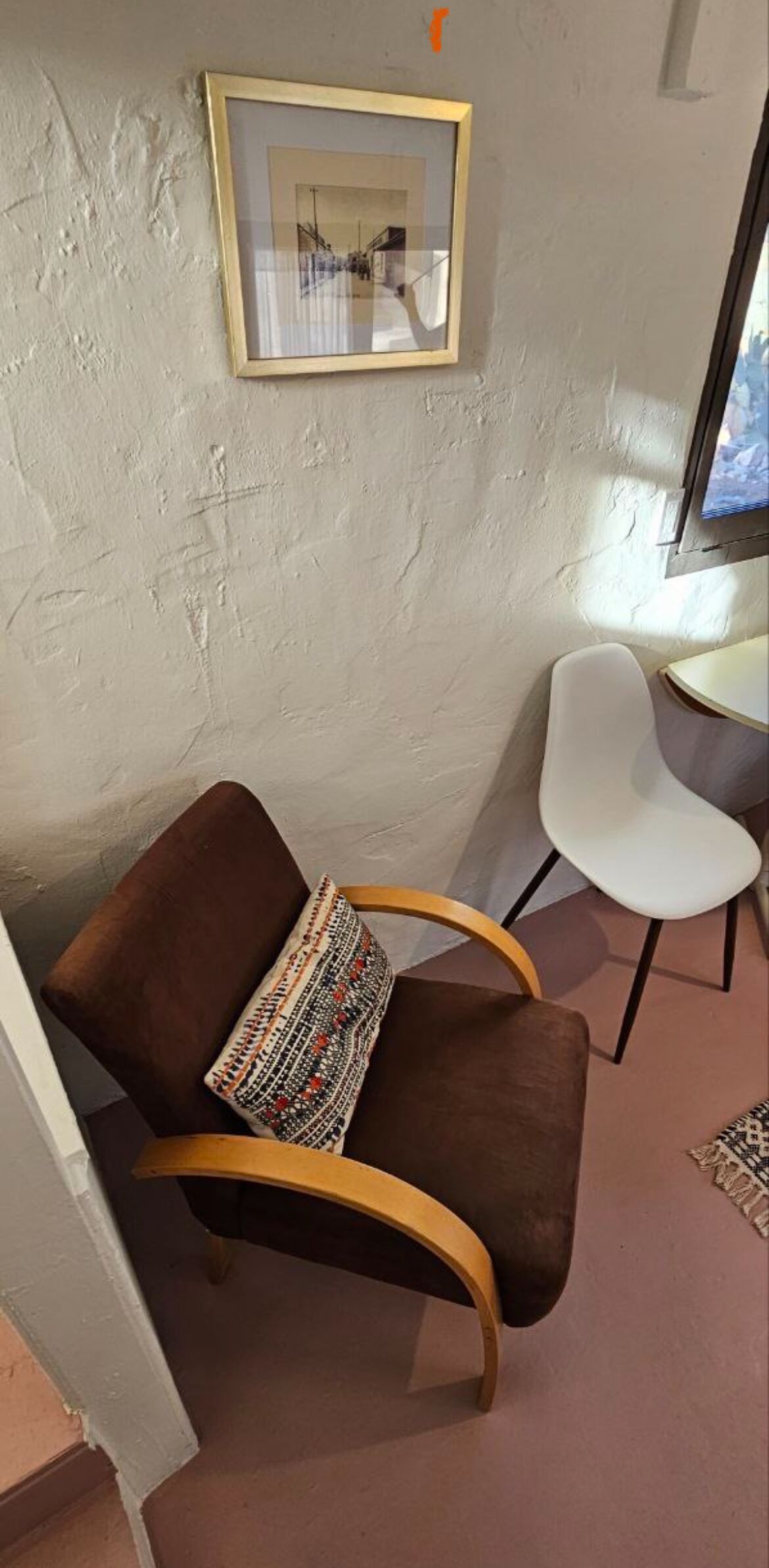 A corner room with a brown chair, a white chair, and a framed picture on the wall.