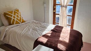 Een slaapkamer met een bed, een raam met gordijnen en een witte muur.