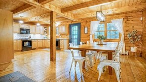 A wooden cabin interior with a dining area, kitchen, and a large window.