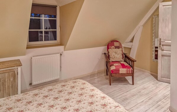 A bedroom with a sloped ceiling, a wooden chair, a radiator, a window, and a door.