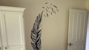 Une chambre à coucher comprenant un lit, une armoire et un motif décoratif représentant une plume et des oiseaux sur un mur.