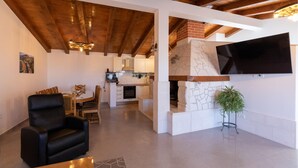 Ein modernes Wohnzimmer mit einer schwarzen Ledersofa, einem Essbereich mit Holztisch und Stühlen, einer Küche mit weißen Schränken und einem Steinkamin sowie einem angebrachten Flachbildfernseher.